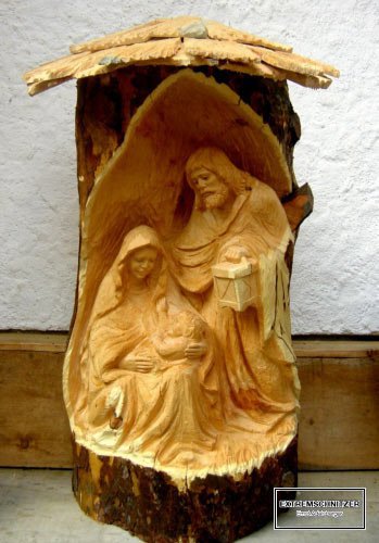 Maria, Josef und Jesus in einer Krippe, die aus einem Holzstamm herausgesägt wurde.